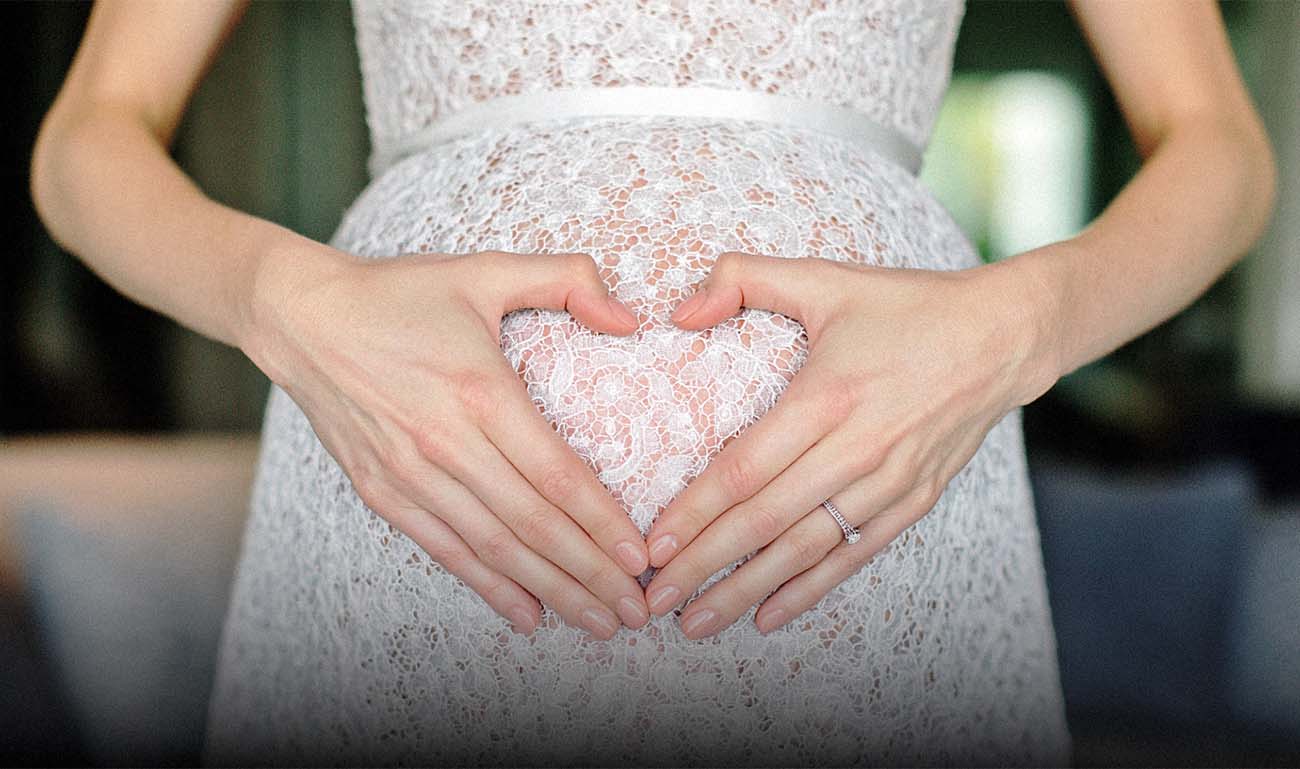 Hände formen ein Herz auf dem Babybauch – schwangere Braut, intime Hochzeitsfotografie Kassel