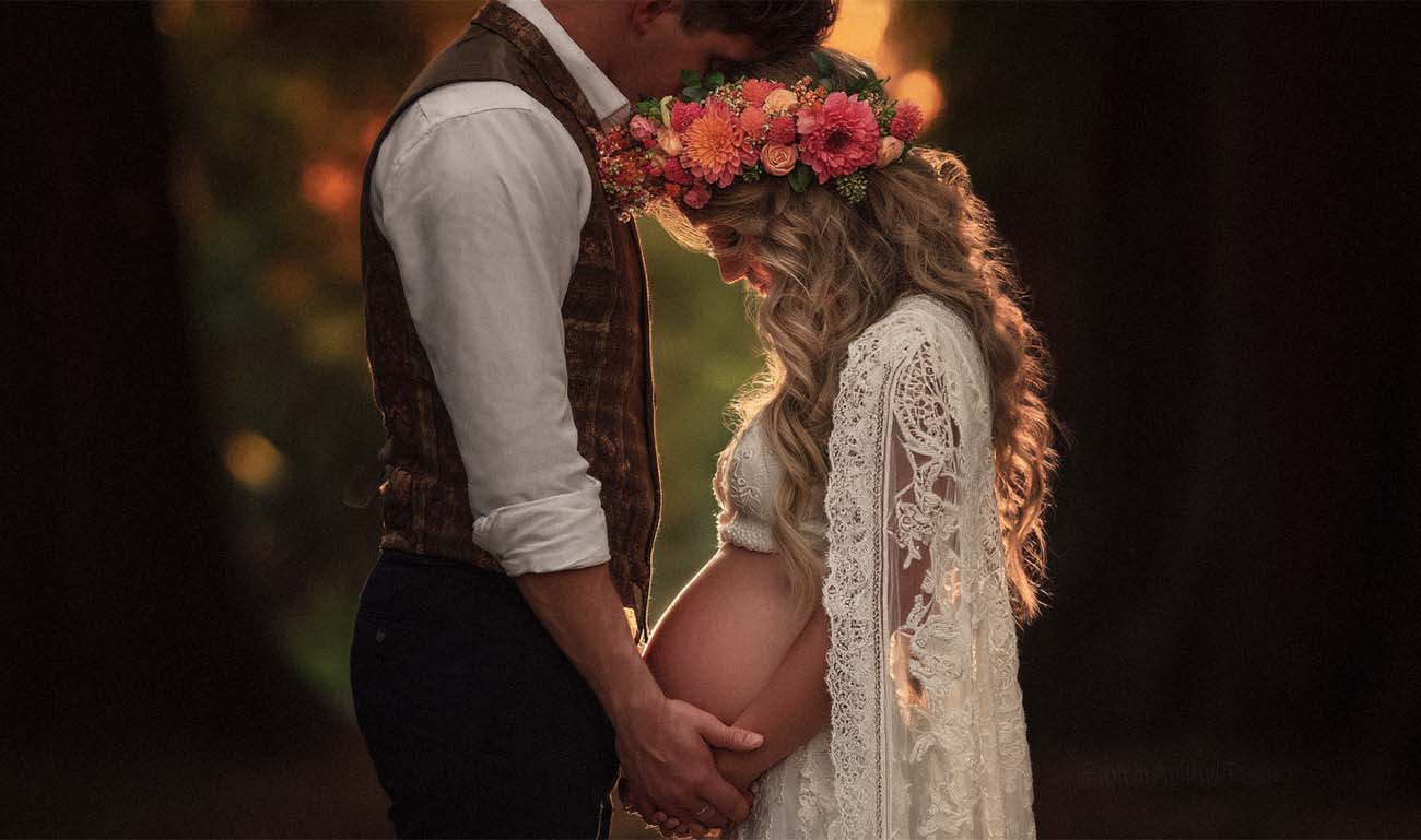 Rustikale Szene: Bräutigam küsst schwangere Braut mit Blumenkranz, Babybauch – Hochzeitsfotograf Kassel
